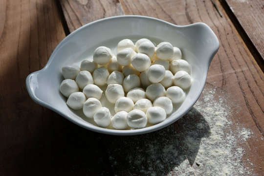 piatto bianco con dentro mozzarelle sopra un tavolo di legno e farina sparsa