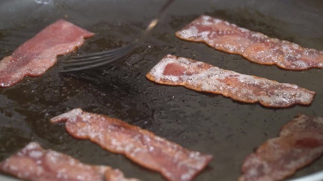 Sizzling hot crispy of bacon pieces being fried in a pan