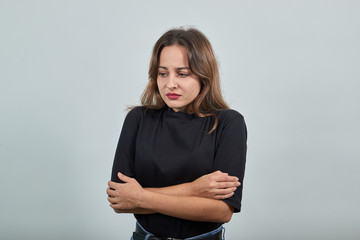 Cute young brunette woman in black t-shirt, blue jeans with belt on gray background, disappointed...