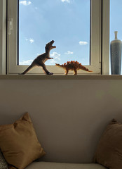 Toy dinosaurs on windowsill with beautiful sky on background