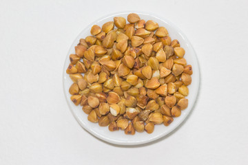 Raw buckwheats on the plate on the white background. Closeup plate with buckwheats.