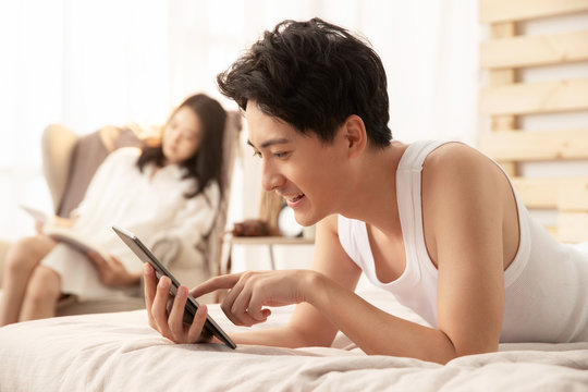 Young husband lying on the bed using tablets