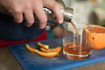 Close up of man pouring orange cocktail into tumbler glass