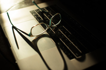 Fototapeta na wymiar eye glasses sitting on top of laptop keyboard in morning sunlight