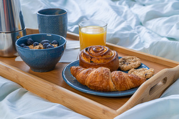 Breakfast served in bed on wooden tray with coffee and croissants