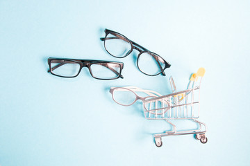glasses for sight and a little shopping trolley, blue background, copy space, online purchase of...