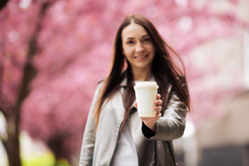 Young beautiful woman with long dark hair enjoys the beauty of spring nature near the flowering sakura tree