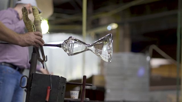 Close-up of glassblower artisan cutting the end of a molten piece of glass extracted from the furnace located in the glass factory where each piece is made manually by the craftsmen. Labour day.