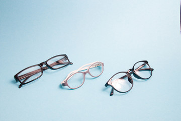 several pairs of different glasses for vision correction on a blue background; copy space, children's glasses and small rivers for adults