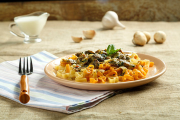A plate of pasta with mushrooms in a creamy sauce with spinach on a linen tablecloth on a napkin and a fork next to milk and mushrooms.