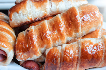 Close-up. Ready-made fried sausages in the dough lie in a pile on a plate.