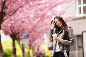 Young beautiful woman with long dark hair enjoys the beauty of spring nature near the flowering sakura tree