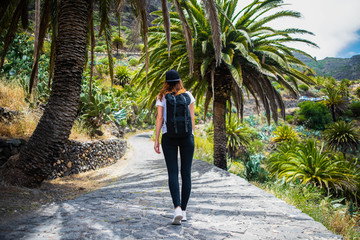 Fototapeta na wymiar Woman walking along a path between palm trees with a backpack on her back