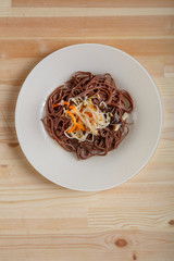 White plate with soba noodles and vegetables from above on a light wooden table.