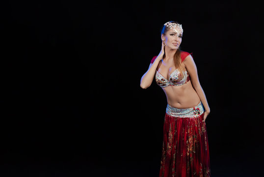 Young woman belly dancer in a red oriental costume on a black background