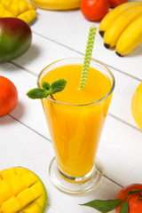 Freshly squeezed mango juice with bananas oranges and tangerines on a sar rustic table. Selected focus.