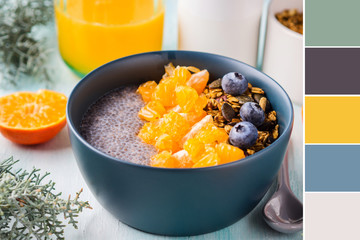 Chia pudding with tangerines and matcha tea granola in a bowl on pastel turquoise wooden background. Plant based breakfast. Color swatch