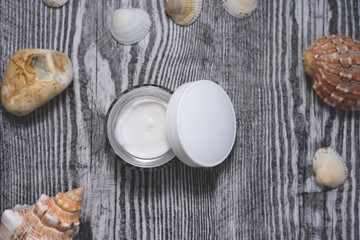 Facial cream and sea shells and stone on the wooden background.