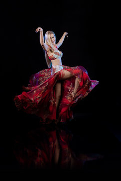 Young woman belly dancer in a red oriental costume on a black background