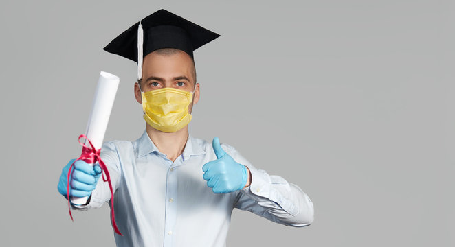 High School Graduation During A Quarantine. Student Graduate In A Hat And A Protective Mask Holds A Diploma And Shows Thumb Up
