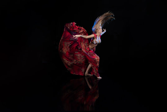 Young woman belly dancer in a red oriental costume on a black background