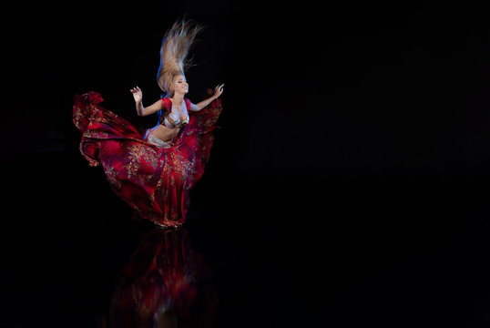 Young woman belly dancer in a red oriental costume on a black background
