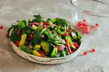 salad vegetable with ruccola, pomegranate seeds, avocado, onions and herbs. Gray concrete background. Thyme. Horizontal orientation