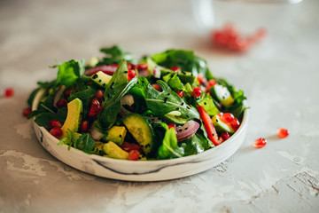 salad vegetable with ruccola, pomegranate seeds, avocado, onions and herbs. Gray concrete background. Thyme. Horizontal orientation