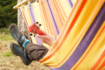 Legs of girl plays the ukulele lying in a colorful hammock. Person plays guitar lying in hammock. Hobby and recreation. Outdoor. Leisure 