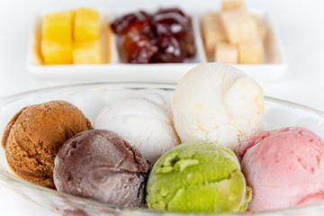 Closeup side view multi colored ice cream in a clear dish and sweet processed fruit for eating together in Thai style, Set of colorful ice cream scoops of different colors on the white table backgroun