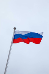 The Russian flag is flying on a flagpole against the sky
