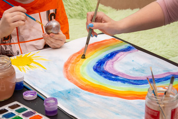 Children draw a rainbow with watercolors on white paper.