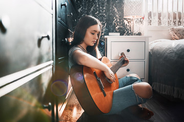 Beautiful teen girl playing guitar in her bedroom