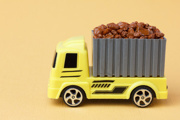 Transportation of bulk concept. Toy yellow truck delivers stones in a container.