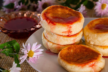 Cottage cheese pancakes with sour cream and jam on a brown background. Breakfast dish next to flowers.