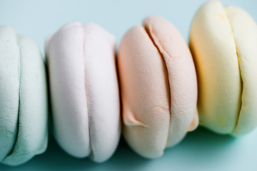 Colored sweet dessert zephyr marshmallows on sky blue background. Air marshmallows. Close up, foof...