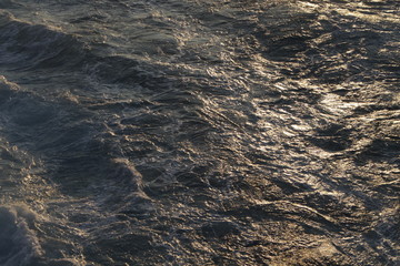 The dark waters of the Mediterranean Sea sway and foam and the waves play with the golden rays of the spring sun.