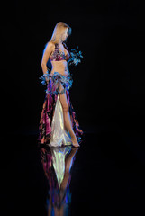 Fototapeta na wymiar Young woman belly dancer in oriental multi-colored costume with feathers on a black background