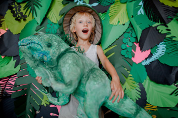 The child holds in his hands an iguana made of papier mache. Child in a traveler hat on a green...