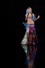 Fototapeta na wymiar Young woman belly dancer in oriental multi-colored costume with feathers on a black background