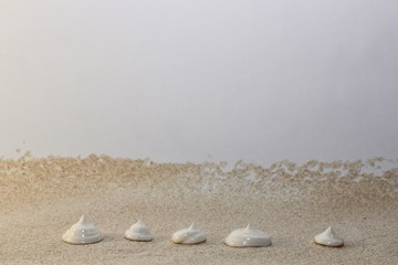 Horizontal background with an embankment of dry sand flour coarse grinding with dosed drops pyramids of light cream.