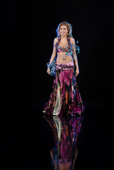 Naklejka na ściany i meble Young woman belly dancer in oriental multi-colored costume with feathers on a black background