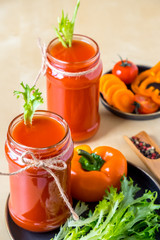two tomato smoothies in a glass jar with the ingredients for its preparation. Fresh tomatoes, carrots, bell peppers and lettuce on a dark plate on a wooden background