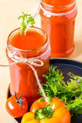two tomato smoothies in a glass jar with the ingredients for its preparation. Fresh tomatoes, bell peppers and lettuce on a dark plate on a wooden background