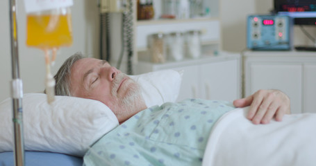 An older adult male hospitalized with coronavirus lying in bed attached to a plasma drip in hopes of helping him fight the disease.