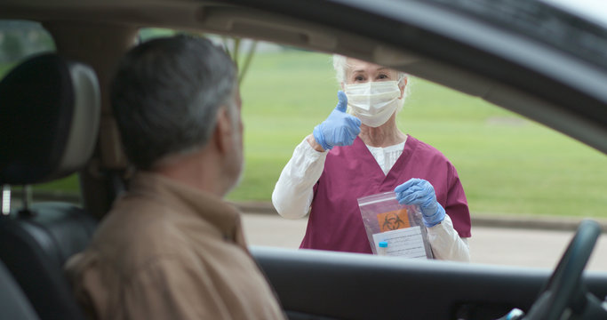 A Mature Man At A Mobile Testing Location Who Has Finished A Do It Yourself Swabbing Procedure Watches A Healthcare Worker Process The Vial That He Has Placed On A Table Outside The Vehicle.