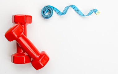 Dumbbell and measure tape in cyan blue color on light yellow background. Sports and healthy lifestyle concept. Barbell next to roll of tape measure. Shaping and fitness equipment, copy space