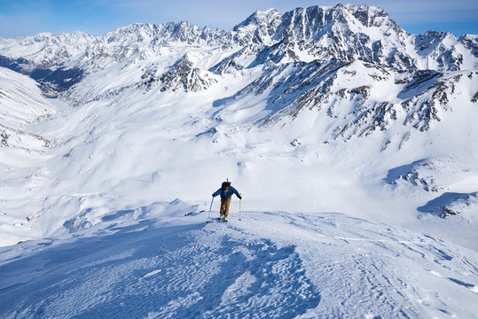 Man ski touring up slow with mountain behind him