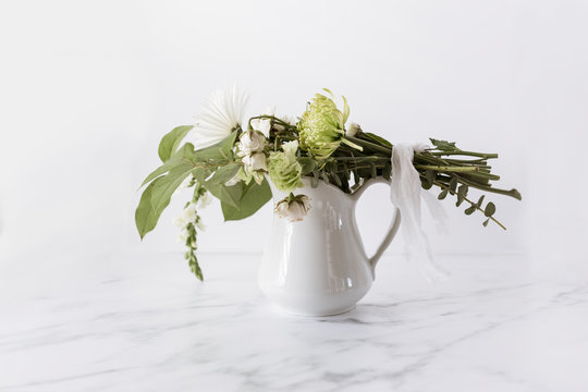 flower bouquet tied with linen ribbon laying on top of white pitcher