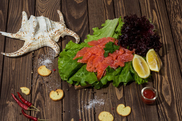 slices of red fish fillet on a wooden background. trout, lettuce, crackers, toasts, red pepper. preparing breakfast